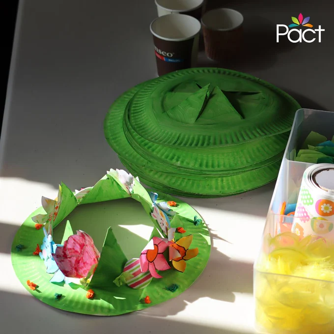 Table of green paper-plate Easter crafts, with craft materials nearby.