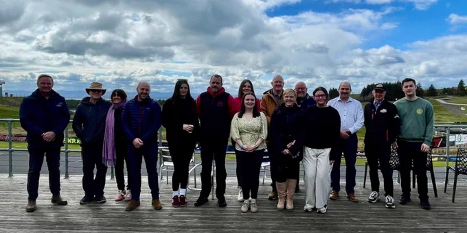 Fifteen people standing in front of a racing circuit.