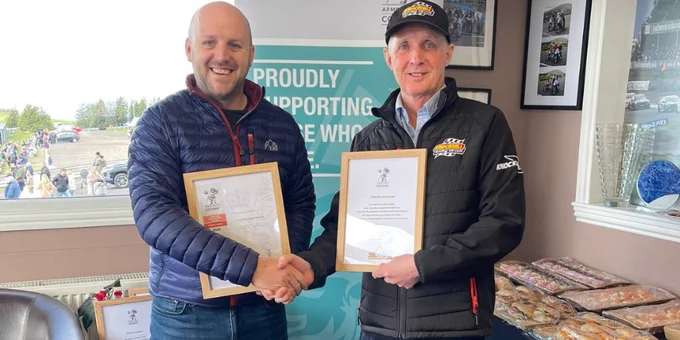 A staff member from J Todd Plant Services holding an Employer Recognition Scheme Bronze Award certificate and shaking hands with Knockhill Racing Circuit's Director of Events who is holding an Armed Forces Covenant certificate.