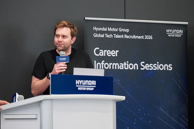 A person stands at a podium holding a microphone, with a banner behind that reads, "Hyundai Motor Group Global Tech Talent Recruitment 2026: Career Information Sessions." The Hyundai Motor Group logo is visible on both the podium and banner.
