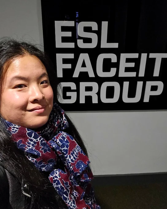 Selfie of Marion smiling in front of a big ESL Faceit Group logo on a wall.