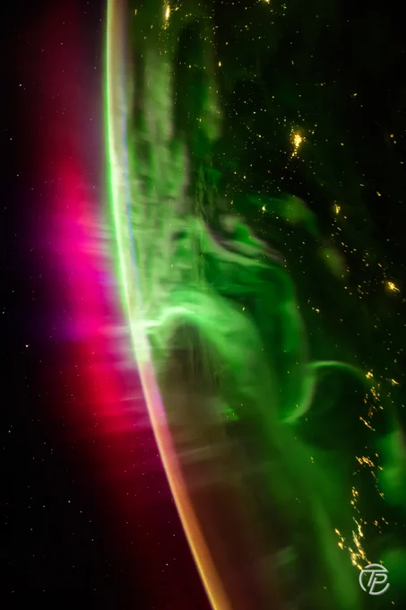 Vue depuis l’orbite de puissantes aurores polaires vertes et rouges ondulant au-dessus de la courbure de la Terre. Les lumières des villes apparaissent en contrebas, tandis que les couleurs de l’atmosphère se mêlent au noir de l’espace étoilé.