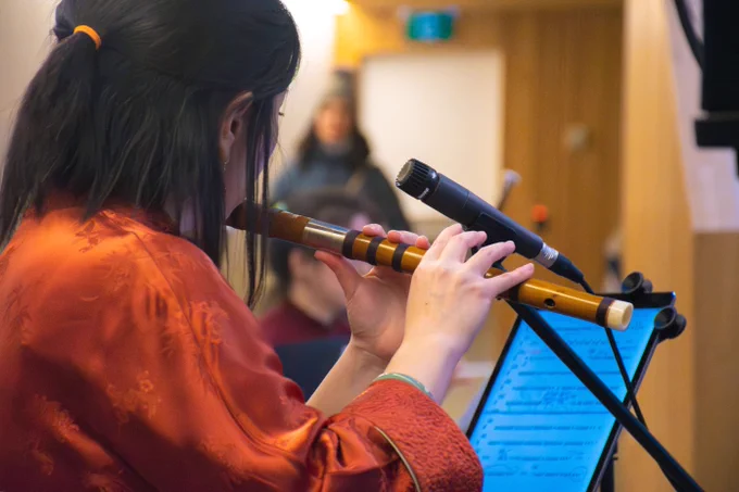 Person performing by playing the flute with a microphone stand to an audience. 