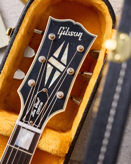 A Gibson Les Paul Custom guitar headstock resting in a plush, orange-lined case.