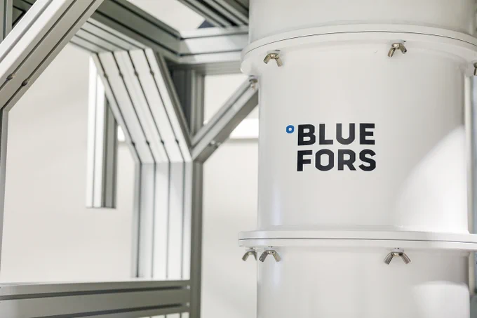 A white cylindrical dilution refrigerator with the Bluefors logo