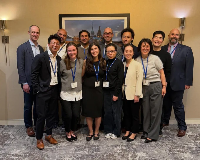 A group of 13 people standing together wearing lanyards and nametags wearing business attire.