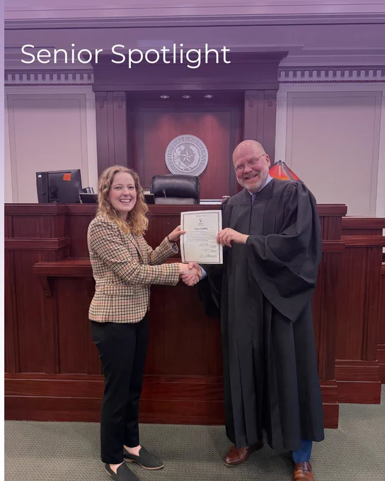 A person in a checkered jacket shakes hands with a judge in a courtroom setting. Both hold a certificate. The background features a judge's bench and a circular emblem on the wall. The text "Senior Spotlight" is visible at the top.