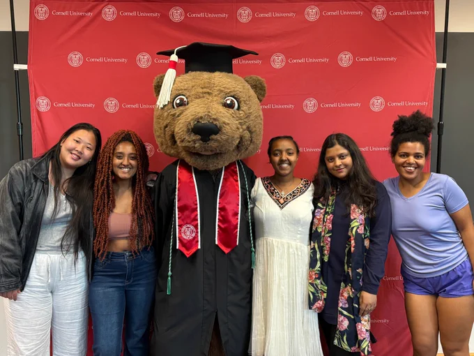International students from the class of 2025 pose for a photo with Touchdown wearing a graduation gown.