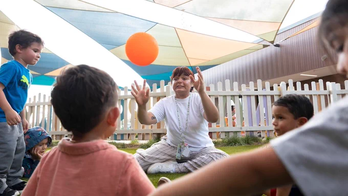 A teacher tossing a ball to a child outside.
