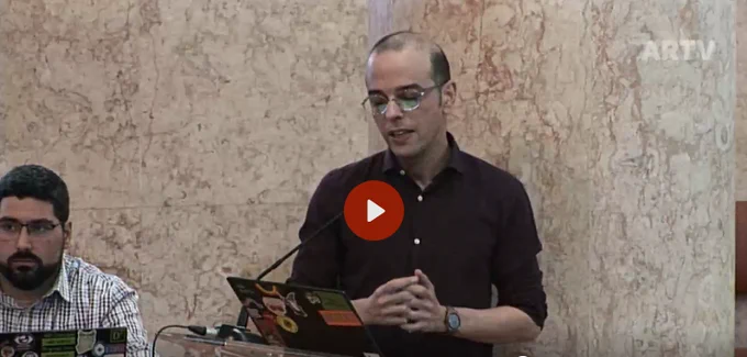 Duas pessoas, uma sentada e outra de pé, num screenshot de um vídeo de uma audição no Parlamento Português, com o logotipo da ARTV no canto superior direito