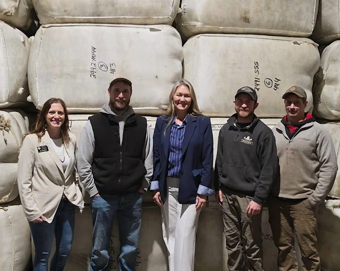A group of five people standing in front of large stacked wool bags at the Center of the Nation Wool  Inc. warehouse.