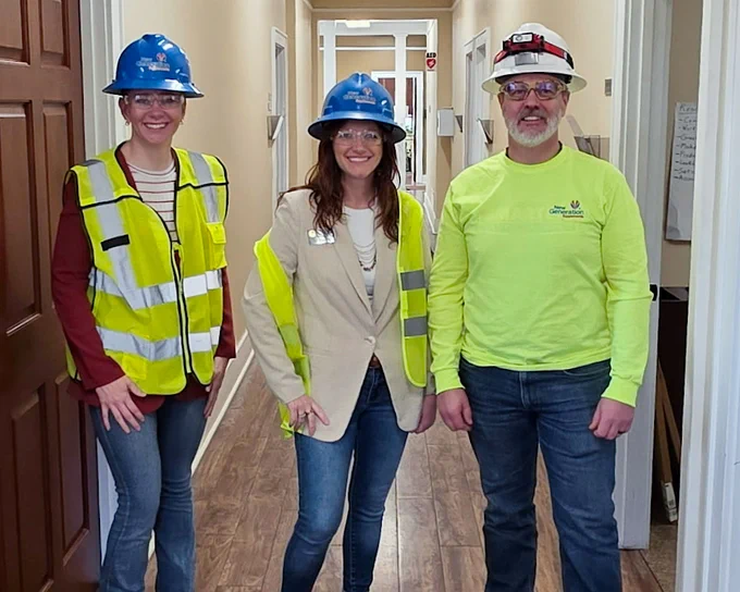 Three people wearing reflective vests, safety goggles, and hard hats stand in a hallway at Next Generation.