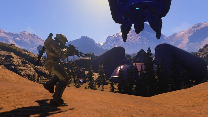 A Spartan runs through sand towards a Covenant war spire in the distance