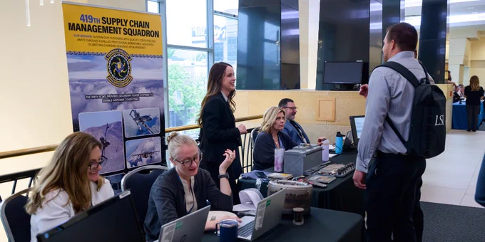 Group of professionals at a 419th Supply Chain Management Squadron recruitment table in a bright lobby area.
