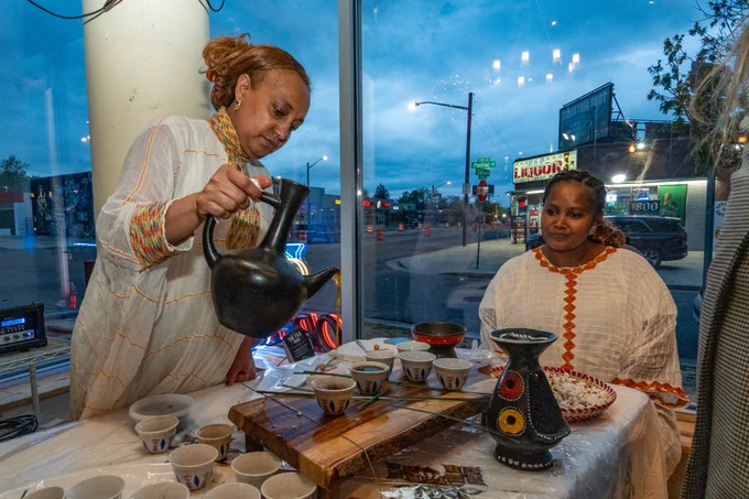 Woman pouring coffee into small cups while another woman watches at a table set with bowls and cups