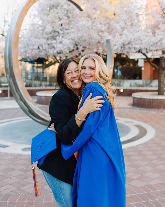 Boise State graduate wearing a graduation robe and hugging their mother. 
