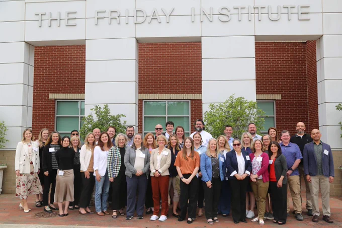 Group photo of professionals standing outside The Friday Institute building under its sign.