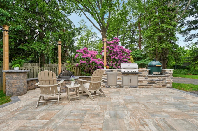 An outdoor patio featuring a grill setup with a Big Green Egg, flower arrangements, and comfortable seating, creating a relaxing garden ambiance.