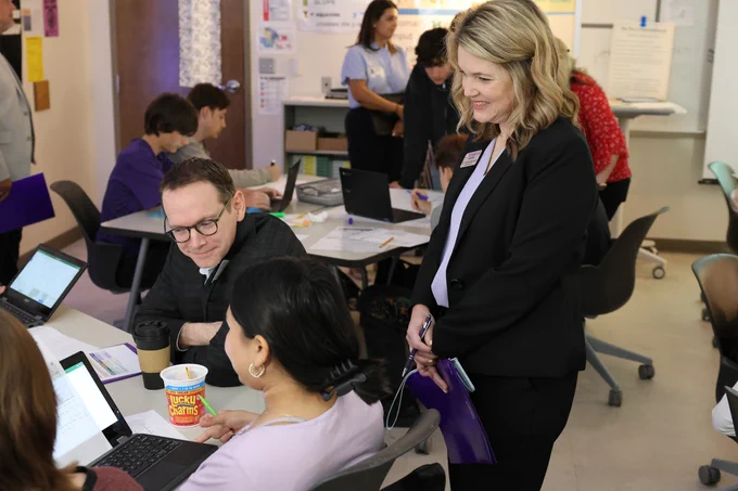 The TEA commissioner and the Granbury ISD superintendent are engaged in a collaborative setting, working on laptops and having discussions with students. 