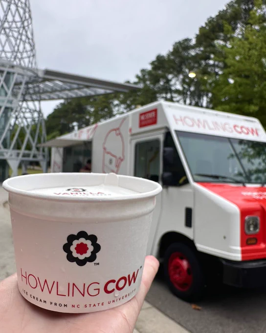 A Howling Cow ice cream cup in the foreground with a red Howling Cow ice cream truck in the background outside of Talley Student Union.