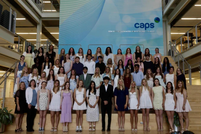 Large group of women and a few men standing in front of the CAPS logo in a building atrium after the students received their pins for becoming CNAs.