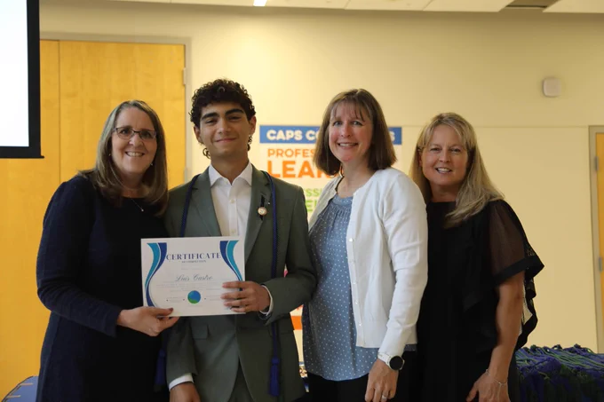 Four people posing for a photo, holding an award or certificate, against a sign that says "CAPS Values".