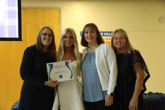 Four women posing for a photo, holding a certificate and smiling.