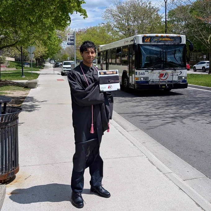 Neel Marathe with his graduation cap in front of a TheRide bus
