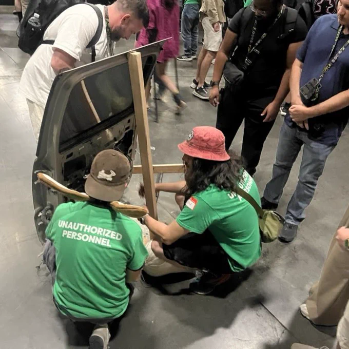 Two physical security village volunteers in green unauthorized personnel shirts showing a demo on a car door