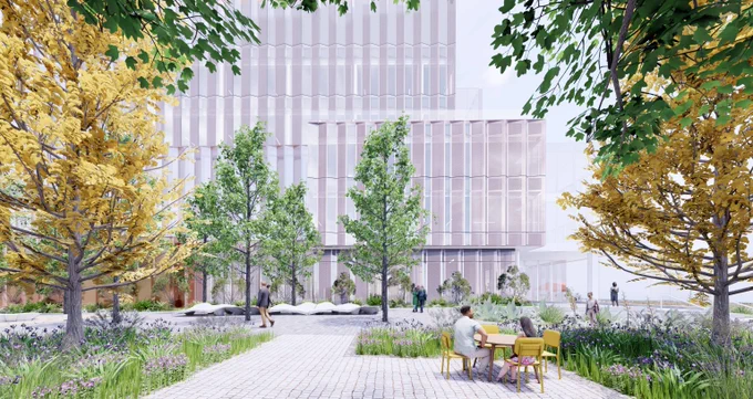 Urban park scene with people walking and sitting at a table surrounded by green and autumnal trees in front of a modern glass building.