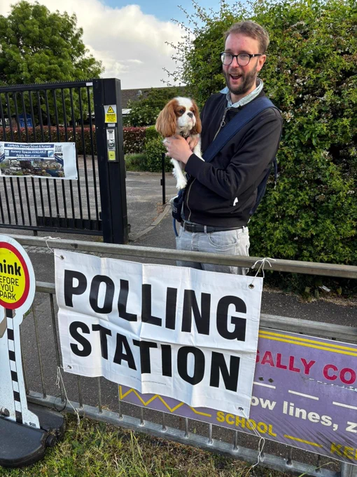 Man with a dog in front of a polling station sign.