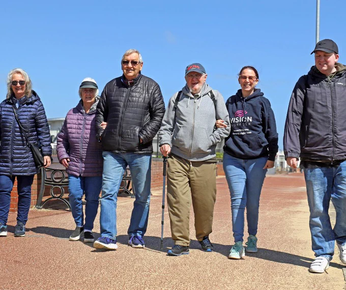 A group of six people walking along the Gorleston promenade on a sunny day.