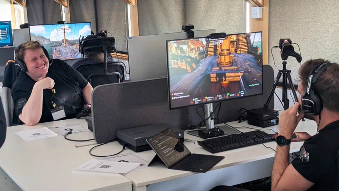 A pair of gentlemen sit at screens playing Sea of Thieves' upcoming Custom Seas game mode. One of them has a wide grin on his face.