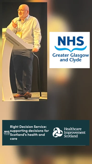 I am stood at a lectern,  walking stick in hand, wearing a blue shirt, blue trousers, brown shoes and glasses. The NHS Glasgow and Clyde and Scotland Healthcare Improvement logos are alongside