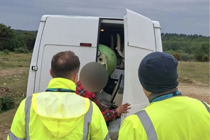 Two people in high visibility jackets look into the back of a white van which is fully loaded waste.