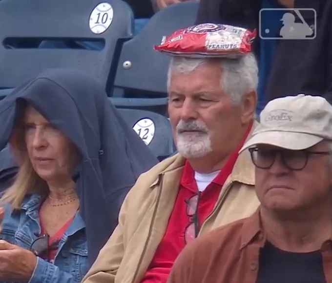 Fan at Nationals Park has a peanuts bag on top of his head. He wears a red polo with a khaki-colored jacket.