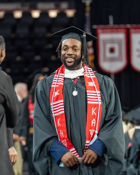 Graduate in black cap and gown wearing a red and white Kappa Alpha Psi stole during a commencement ceremony.