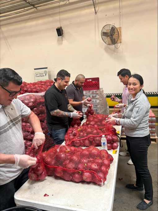 Volunteers wearing gloves sorting and bagging red onions at a food distribution center.