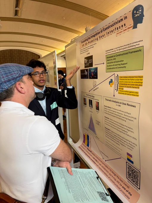A student in a black suit speaking about his poster with his left hand to a judge in a white shirt and blue checked newsboy hat.