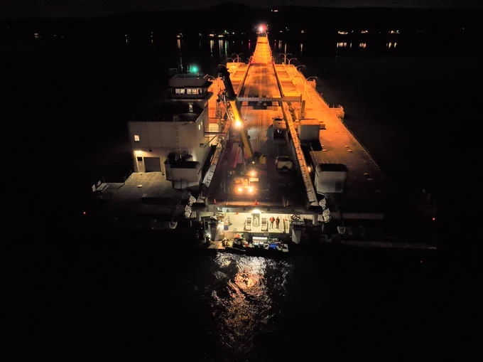 The SR 104 Hood Canal Bridge at night. The bridge is open with workers beneath the bridge and a crane sitting on the roadway above.
