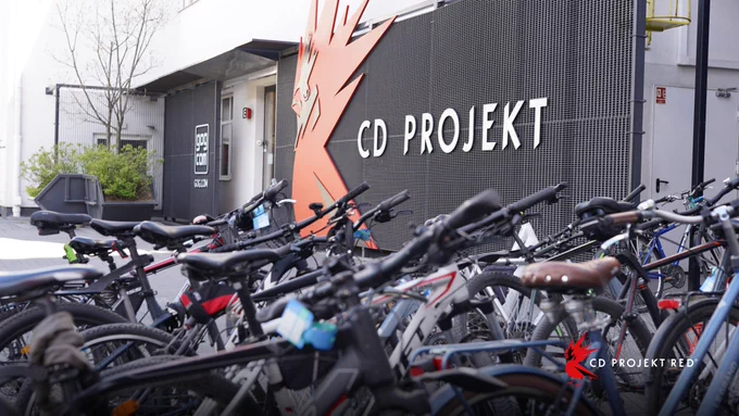Several push bikes lined up outside the entrance to the CD Projekt Red Headquarters in Warsaw. The company name is affixed outside the entrance next to a stylized large red rarog bird.