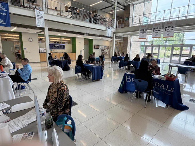 Lobby of a busy building with people sitting at tables, signs, and an entrance visible.