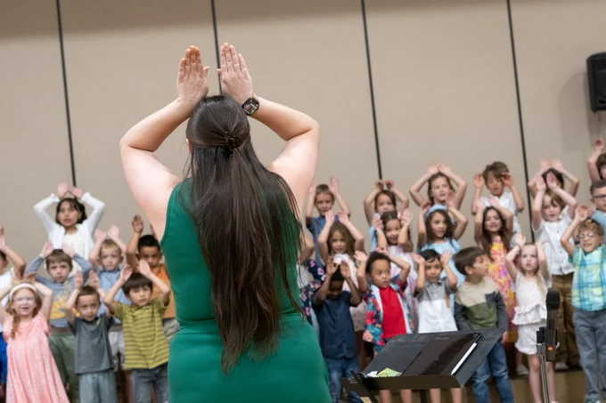 Teacher leading a large group of kindergartners in choreography during their end of the year concert