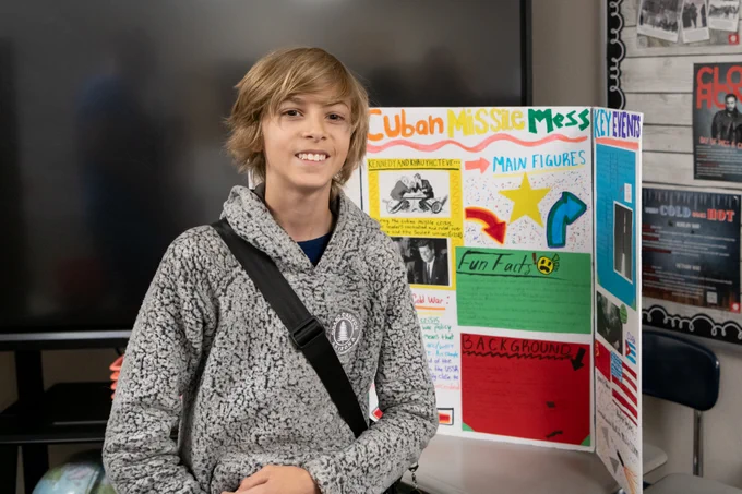 Student presenting a colorful trifold board about the Cuban Missile Crisis in a classroom setting.