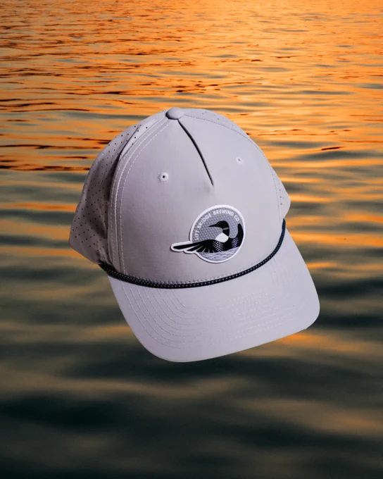 A sleek white cap with a logo, set against a serene sunset over water. The mood is relaxed and tranquil.