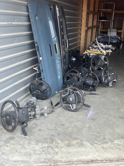 A storage unit contains several steering wheels, a vehicle door, and other automotive parts scattered on a concrete floor.