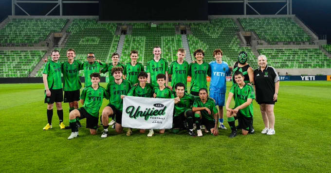 A group of people in green soccer uniforms stands on a field, holding a banner reading "Unified Football, Presented by Jabil". 
