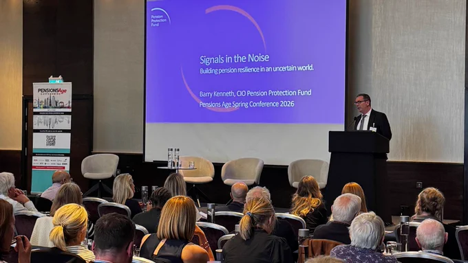 Our CIO stands at a podium speaking to an audience at a conference. On the screen is a presentation titled "Signals in the Noise: Building Pension Resilience in an Uncertain World" by Barry Kenneth, CIO of the Pension Protection Fund. The setting is a large conference room with attendees seated and listening attentive.