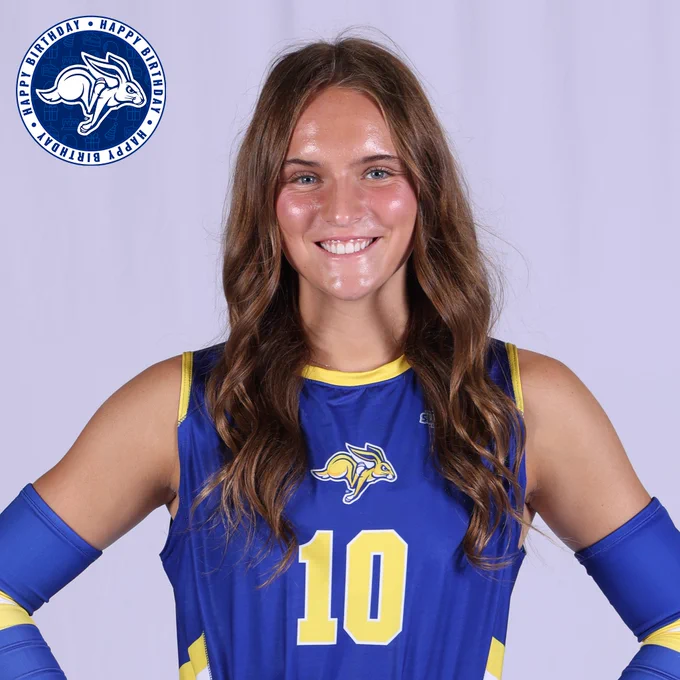 Studio portrait of a South Dakota State volleyball athlete wearing a blue jersey with the number 10 and blue arm sleeves, standing against a white background with hands on hips. A circular “Happy Birthday” graphic with the Jackrabbits logo appears in the top corner.