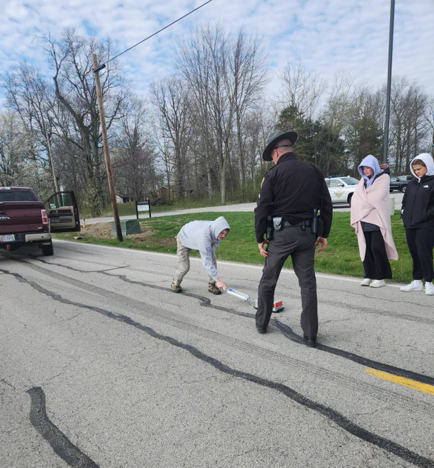 A trooper is explains crash reconstruction with a student as others watch. They are standing on a road.